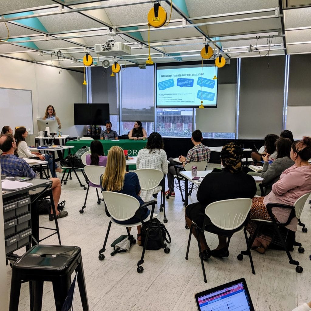 Attendees of the October 2019 Taylor Social Innovation Conversation sit in the Taylor Classroom listening to the presenters speak at a table.