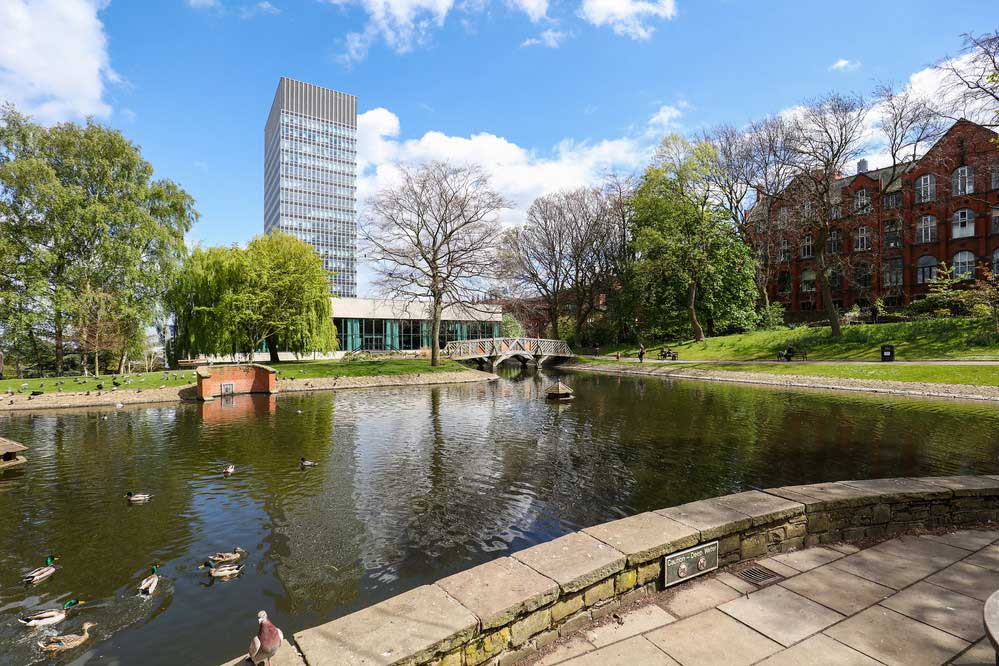 A view of the buildings, lawn, trees and water feature of the Sheffield University Management School.