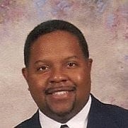 Leroy Divinity smiling wearing a dark jacket and white shirt.