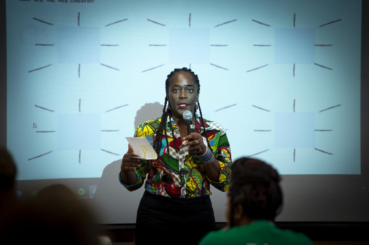 Lesley-Ann Noel speaking into a microphone and wearing a colorful shirt.