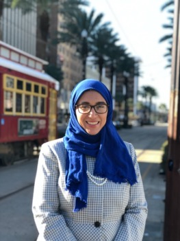 A person wearing a blue head scarf and glasses smiling for the camera