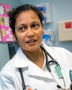 fit clinic anjali niyogi A female doctor anjali niyogi wearing a white coat and stethoscope speaks with a patient in a medical examination room. The doctor appears engaged and focused, and there are medical posters and equipment in the background.